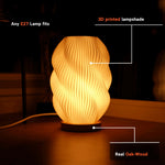 Helix 3D printed table lamp with spiral design and oak wood base glowing warmly on a window sill.