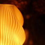Helix 3D printed table lamp with spiral design and oak wood base glowing warmly on a window sill.
